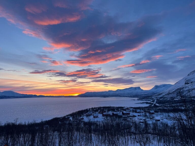 Coucher de soleil à Abisko en Laponie suédoise, illuminant un lac gelé recouvert de neige blanche à perte de vue