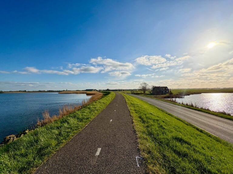 Piste cyclable ensoleillée traversant le Waterland aux Pays-Bas, entourée d’eau des deux côtés, lors d’une journée à vélo